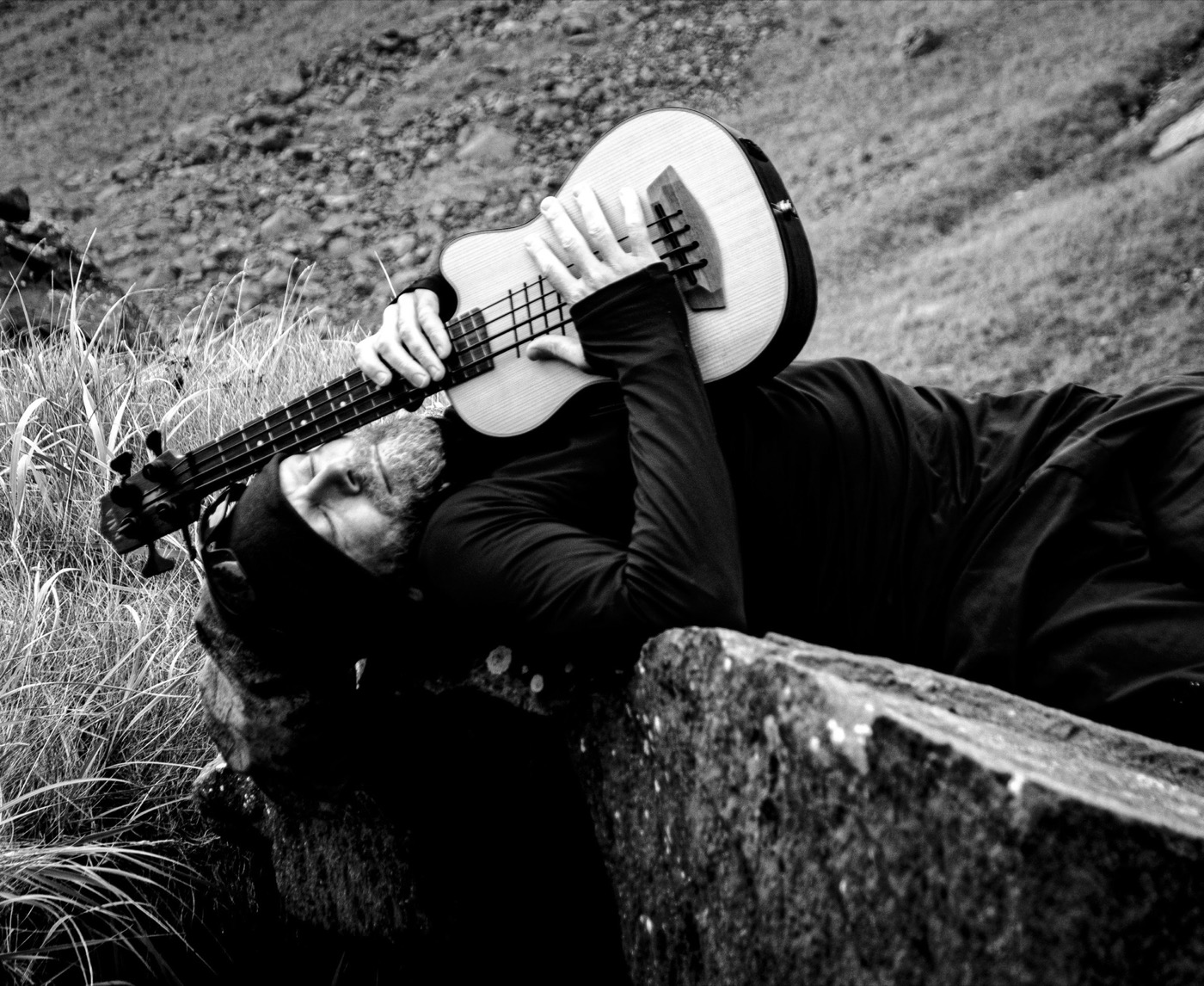 Allongé dans l’herbe contre un rocher, une guitare basse serrée contre soi.